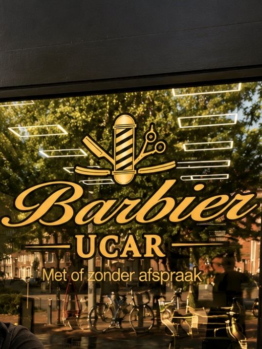 Het gouden Barbier Uçar-logo op de etalageruit, met barberspaal.